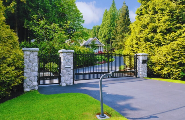 Automatic driveway gate with stone pillars and landscaped greenery, enhancing home security, privacy, and modern curb appeal. Automatic driveway gate with stone pillars and landscaped greenery, enhancing home security, privacy, and modern curb appeal.