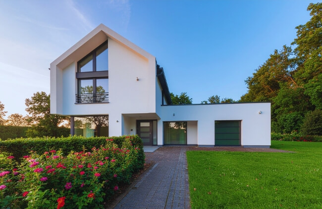Modern home exterior with a paved driveway and landscaped garden beds that frame the driveway with greenery. Modern home exterior with a paved driveway and landscaped garden beds that frame the driveway with greenery.
